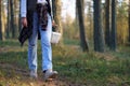 Woman in jeans walks holding basket of mushrooms among trees closeup crop body