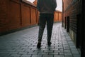 A woman in jeans walks through the narrow streets of the old city. Cropped photo back view of legs. Brick walls around the Royalty Free Stock Photo