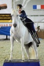 Woman jockey in blue dress International Horse Show. Female rider on a white horse. Riding hall