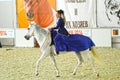 Woman jockey in a dark blue dress riding a white horse. During the show. International Equestrian Exhibition