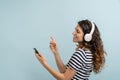 Woman joyful wearing wireless headphones listening to music, holding mobile phone in hand, dancing