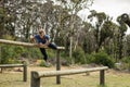 Woman vaulting over wooden beam in clearing on obstacle course wearing blue top, black leggings Royalty Free Stock Photo