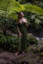 Woman in jungle standing under the fern, wearing green dress. Caucasian woman walking in tropical rain forest. Nature concept.