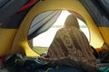 Woman just woken up in camping tent, wrapped in wool blanket and admiring sunrise on the river. Local travel on nature, trekking, Royalty Free Stock Photo