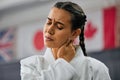 Woman karate student with bad neck pain at fitness training studio, person holding head from sport injury at health gym