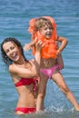 Woman keeps in hands girl in lifejackets in sea