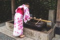 Woman in kimono rinsing hands at Japanese purify water fountain, called chozubachi, at Fushimi Inari shrine, Kyoto, Japan