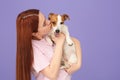 Woman kissing cute Jack Russell Terrier dog on violet background. Space for text Royalty Free Stock Photo