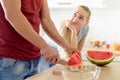 Woman in a kitchen eating red watermelon and looking at her husband, Couple in their large contemporary white kitchen