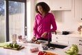 Woman In Kitchen At Home Wearing Fitness Clothing Blending Fresh Ingredients For Healthy Drink