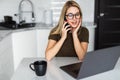 Young woman with laptop using cellular phone in the kitchen Royalty Free Stock Photo