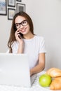 Young Woman in kitchen with laptop using cellular phone smiling in the morning Royalty Free Stock Photo