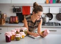 Woman in kitchen listing ingredients in vegetable preserves