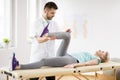 Middle age woman with knee injury lying on physiotherapy table during session with young handsome doctor Royalty Free Stock Photo