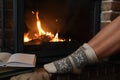 Woman in knitted socks resting near fireplace, closeup. Winter vacation