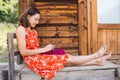 Woman is knitting from pink yarn on the veranda of a wooden house