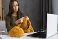 Woman with knitting yarn and needles learn how to knit using website on a laptop at modern home in winter day. Royalty Free Stock Photo