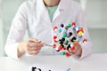 Woman in laboratory coat demonstrates model of molecule