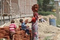 Woman Laborer holding bricks on her head her children helping her to bring up the bricks while working on a construction site near
