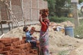 Woman Laborer holding bricks on her head her children helping her to bring up the bricks while working on a construction site near