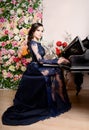 Woman in lace deep blue dress playing the piano and flowers. Retro vintage style Royalty Free Stock Photo