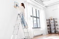 woman on ladder decorating home with art