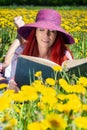 Woman, lady with long red hair in a meadow with dandelions, reads a book