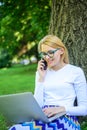 Woman with laptop in park order item on phone. Girl takes advantage of online shopping. Girl sit grass with notebook Royalty Free Stock Photo