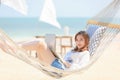 Woman laying on fabric swing on sand beach and using laptop notebook computer working and looking to camera with happy face. Royalty Free Stock Photo