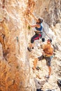 Woman lead climbing on natural cliff, guy belayer watching her Royalty Free Stock Photo