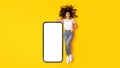 Woman Leaning On Big Cellphone With Empty Screen, Yellow Background Royalty Free Stock Photo