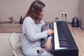 A woman learns to play the piano while sitting in a home kitchen next to a cat