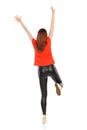 Woman In Leather Trousers And Orange Shirt Is Standing On One Leg With Arms Raised. Rear View. Royalty Free Stock Photo