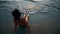 Woman legs and bare feet sitting on golden sand beach at sunset and looking at ocean water Royalty Free Stock Photo