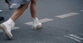 Woman legs crossing street on crosswalk with crowd in city background.