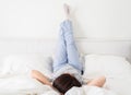 Woman with legs raised up high and arms under her head lying on bed in bedroom Royalty Free Stock Photo