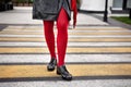 Woman legs in red color tights, black leather shoes with rivets and skirt stand on crosswalk. Fashion details for