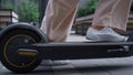 Woman legs riding kickscooter in white sneakers going away at downtown closeup.