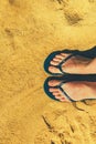 Woman legs in slippers on yellow sand background. Blue flip flops on beach. Copy space, top view. Holiday and travel Royalty Free Stock Photo