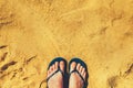 Woman legs in slippers on yellow sand background. Blue flip flops on beach. Copy space, top view. Holiday and travel Royalty Free Stock Photo