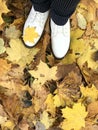 Woman legs in white autumnal shoes. Standing on a carpet of yellow autumn leaves. Filmed from above