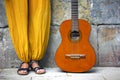 Woman legs with yellow hippie pants and black sandals next to acoustic vintage guitar on a square on stone background. Free happy Royalty Free Stock Photo