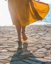 woman legs in yellow sundress walking to sea by stone beach Royalty Free Stock Photo