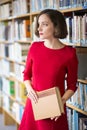 Woman in library with book looks away