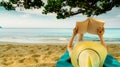 Woman lie down on green towel that put on sand beach under the tree and reading a book. Slow life on summer vacation. Asian woman