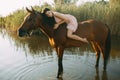 Woman lies astride a horse at river