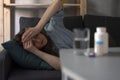 Woman lies on couch and holds head with hands, pills on the table. Headache, migraine, hangover