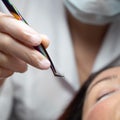 Woman lies on eyelash extension procedure in a beauty salon. Lashmaker holds tweezers with a bunch of artificial