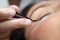 Woman lies on eyelash extension procedure in a beauty salon. Lashmaker holds tweezers with a bunch of artificial