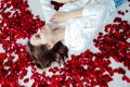 a beautiful woman lies in the flowers of the petals of red roses Royalty Free Stock Photo